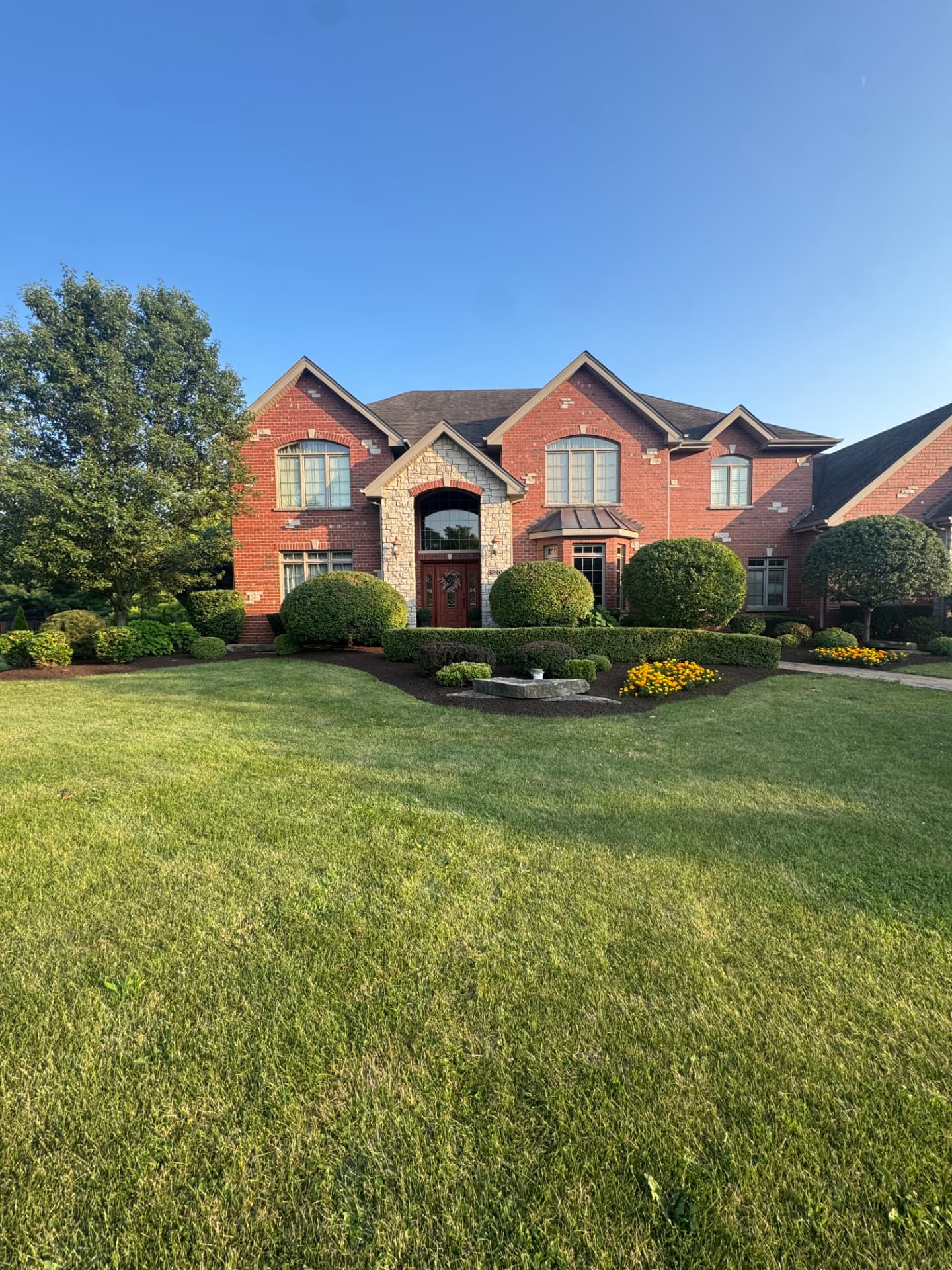Brick home front yard with trimmed shrubs, fresh mulch beds, and a manicured lawn.